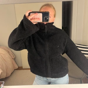 Svart teddyjacka hm - Mysig svart teddyjacka med hög krage och hel dragkedja framtill. Jackan har två stora fickor och är tillverkad i fluffigt fleece-material som ger en chill och avslappnad vibe. Perfekt att slänga på sig när det är kallt ute.💕