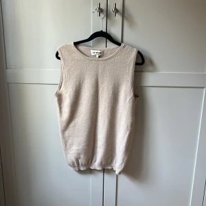 Beige kashmirväst från Soft Goat XS - Minimalistisk beige väst i 100% kashmir från Soft Goat. Modellen är ärmlös med rund halsringning och ribbad nederkant. Perfekt för lager-på-lager och ger en clean look till din outfit.