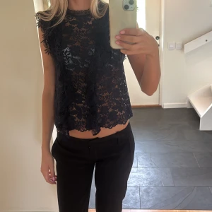 Mörk blå spetsblus  - Säljer en mörk blå, ärmlös blus i genombruten spets med blommigt mönster. Toppen har rund halsringning och lätt croppad passform. Perfekt för dig som gillar detaljer och en feminin look.