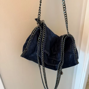 Mörkblå axelväska med kedjedetaljer - Säljer en snygg mörkblå axelväska som liknar Stella McCartney med coola silverfärgade kedjor längs kanterna och som axelrem. 