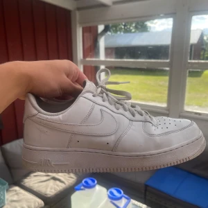 Nike Air Force 1 vita sneakers - Klassiska Nike Air Force 1 sneakers i helvitt skinn med perforerad tå, rund tå och platt sula. 
