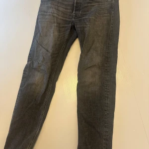 Svarta tapered jeans Jack & Jones - Snygga svarta jeans från Jack & Jones i modellen Tapered/Mike. Jeansen har en tvättad look med lätt slitning, klassiska fem fickor och smalare ben. Perfekta för dig som gillar en avslappnad men ändå stilren vibe. Minimalt slitage, storlek är 41/42