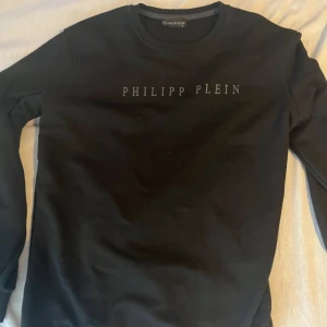 Svart sweatshirt från Philipp Plein - Svart sweatshirt från Philipp Plein med stilren logotyp i relief över bröstet. Klassisk rund halsringning och långa ärmar. Tröjan har en clean look och är tillverkad i mjukt material som känns skönt mot huden. Storlek L men passade mig som har M också.