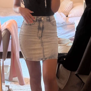 Ljusblå jeanskjol med hög midja - Säljer en ljusblå jeanskjol med hög midja och klassiska fickor både fram och bak. Kjolen är kort och har en figurnära passform som framhäver siluetten. Perfekt till sneakers eller boots för en cool look.