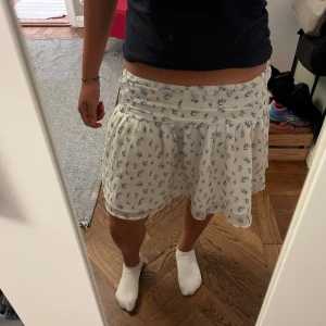 Vit blommig kjol från Gina Tricot - Supersöt vit kortkjol från Gina Tricot med blått blommönster. Den är använd för länge sen! Den har en sminkfläck som tyvärr inte går bort i tvätten men fläcken på självaste kjolen är ljus/svag så syns inte jättemycket men fläcken på tyget innanför kjolen syns däremot mer💕