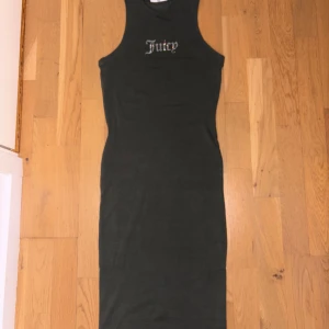 Svart långklänning Juicy Couture - Snygg svart långklänning från Juicy Couture med ärmlös design och rund hals. På bröstet står det 'Juicy' i glittriga paljetter som ger en extra touch. Klänningen är figurnära och gjord i mjuk bomull, perfekt för dig som gillar stilren och trendig look.