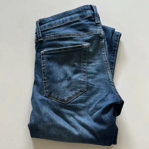 Slim fit jeans från Jack & Jones - Snygga blå jeans från Jack & Jones i modellen Slim/Glenn. De har en slim passform med raka ben och klassisk femficksdesign. Jeansen är tillverkade i mjukt denimtyg med lite stretch för extra komfort. Perfekt för dig som gillar en stilren och modern look. Det är storlek 29 i midjan men den passar 30-31