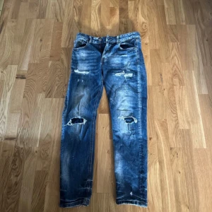 Blå slitna jeans Supply & Demand - Riktigt snygga blå jeans från Supply & Demand med slitna detaljer och hål på knäna. Jeansen har klassisk femficksdesign, raka ben och cool tvättad look. Perfekta för dig som gillar streetstyle och vill sticka ut lite extra.