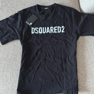 Svart DSQUARED2 t-shirt i bomull - Svart t-shirt från DSQUARED2 med vit logga tryckt över bröstet. Klassisk passform med rund halsringning och korta ärmar. Tillverkad i mjuk bomull, perfekt för en clean och stilren look.