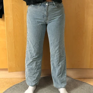 Blå jeans med rosa rosetter - Säljer ett par ljusblå raka jeans med normal passform. På bakfickorna finns broderade rosa rosetter som ger en söt och unik touch. Jeansen har klassisk femficksdesign och är tillverkade i mjukt bomullsjeans. Perfekta för dig som vill ha något extra i din denimstil.