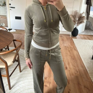 Olivgrön velourväst från Juicy Couture - Säljer en olivgrön velourväst från Juicy Couture med huva, guldfärgade detaljer på dragkedja och snören samt broderad JC-logga på bröstet. Byxorna är i storlek M och koftan i xs🫶🏽🩷 använt två gånger
