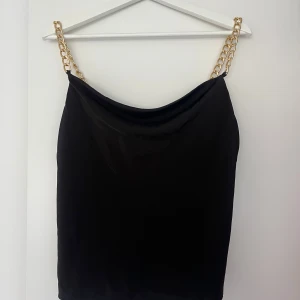 Svart linnetopp med gulddetaljer - Svart linnetopp med sateneffekt och gulddetaljer från Amisu