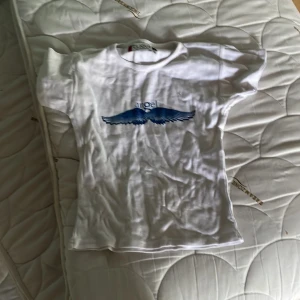Vit t-shirt med blått tryck från Clique - Vit t-shirt från Clique i storlek S med ett blått tryck av vingar och texten 'angel' på bröstet. Sitter tajt 