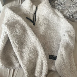 Vit fleece half zip från Seven Cities - Supermjuk och fluffig vit fleece-tröja från Seven Cities med half zip och hög krage. Perfekt för kyliga dagar, riktigt cozy vibe. Långärmad modell med relaxed fit och svart dragkedja som detalj. Snygg att slänga på sig över allt.