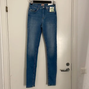 Blå skinny jeans från ONLY S/34 - Snygga skinny jeans från ONLY i mellanblå denim. Modellen är midwaist med klassisk femficksdesign och smal passform hela vägen ner. Perfekta för dig som gillar en tight look och vill ha ett par stilrena jeans till vardags. Materialet är mjukt och stretchigt för extra komfort. (Aldrig använda)
