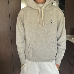 Grå hoodie från Polo Ralph Lauren - Snygg ljusgrå hoodie från Polo Ralph Lauren med klassisk broderad logga på bröstet. Tröjan har huva med snörning, känguruficka och är tillverkad i mjuk bomullsmix. Perfekt för chill dagar eller när du vill ha en clean och enkel look.storlek liten medium