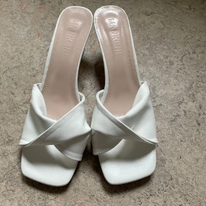 Vita klackade sandaler från Mankeni - Snygga vita klackar med låg klack och trendig fyrkantig tå som gör de lätta och sköna att gå i. Skorna har breda korslagda remmar i syntetmaterial och öppen häl, vilket ger en modern och stilren look. Perfekta för att lyfta din outfit med en chic touch. De är helt oanvända och säljer för de tyvärr är för små. Tycker själv de är väldigt söta och passar till allt, väldigt sköna också! 