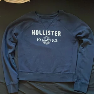 Mörkblå Hollister sweatshirt XS - Mörkblå sweatshirt från Hollister i storlek XS. Tröjan har broderad logga och text framtill med 'Hollister 1922 Del Mar Surf Academy'. Klassisk rund halsringning och långa ärmar. Perfekt för en chill och avslappnad stil.