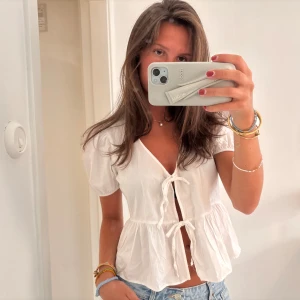 Vit blus med knyt från Bershka - Supersöt vit blus från Bershka med puffärmar, v-ringning och två knyt framtill. Modellen är lite croppad och har volang nedtill för en extra feminin touch. 