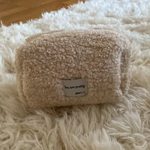 Beige fluffig necessär från Gina Tricot - Supermjuk och fluffig necessär i beige teddy-material från Gina Tricot. Rektangulär form med dragkedja upptill och etikett framtill med texten 'You are pretty'. Perfekt för smink eller småprylar när du är på språng.