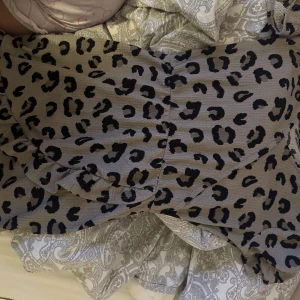 Leopardmönstrad kortklänning - Säljer en snygg kortklänning med leopardmönster i svart på grå botten. Klänningen har en figurnära passform och är perfekt för dig som vill sticka ut. Materialet känns mjukt och följsamt mot kroppen. Perfekt för dig som gillar djurmönster och trendiga looks.