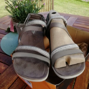 Grå sandaler från Merrell strl 42 - Snygga sandaler från Merrell i grått med  remmar och diskret mönstrade band. Modellen District Mendi Backstrap har en mjuk fotbädd och ljus sula, perfekt för varma dagar. Passar dig som vill ha både stil och komfort. Sandalerna endast provade, aldrig använda. Inköpspris, 1100kr  men säljs för mindre än halva inköpspriset! 