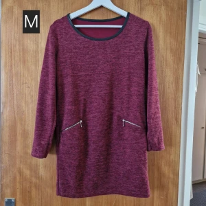 Vinröd långärmad klänning M - Vinröd klänning i mjukt material med lång ärm och två sneda dragkedjor framtill. Enkel, rak modell med rund halsringning och svarta kantdetaljer. Perfekt för dig som gillar stilren och bekväm look.