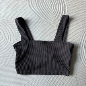 Svart ribbad linnetopp - Snygg svart ribbad linnetopp med breda axelband och croppad passform. Perfekt att styla med höga jeans eller kjol för en trendig look. Enkel och stilren design som passar till många outfits.