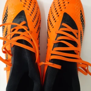 Adidas Predator orange fotbollsskor - Snygga Adidas Predator fotbollsskor i orange och svart med coola detaljer och snörning. Skorna har mönstrad ovandel och dobbar för bästa grepp på planen. Tillverkade i syntetmaterial och designade för att sticka ut på matchen. Knappt använda. Använt runt 10 gånger