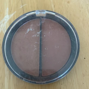 Duo bronzer & rouge från Glam of Sweden - Snygg duo med bronzer och rouge i en oval dosa från Glam of Sweden. Ena sidan är en varm brun bronzer, andra sidan ett rosabrun rouge. Perfekt för att skulptera och ge färg till ansiktet. Kompakt puderformat, lätt att ta med i väskan.