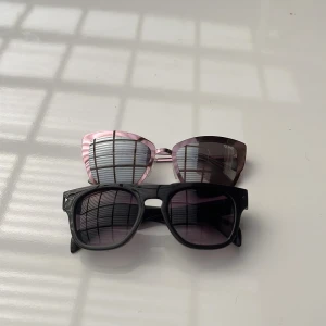 Två par solglasögon från QUAY AUSTRALIA - Ett par mörka solglasögon med svart båge och mörk lins kallas ENCOUNTER 4.2 , Ett par kattformade glasögon som är rosguld metalliska och en ljus lins kallas SUPERGIRL kan diskutera priser