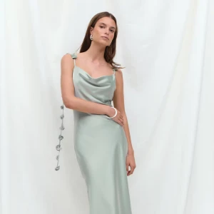 Ljusgrön långklänning i satin - Superfin ljusgrön långklänning i satin med smala axelband och draperad urringning. Klänningen har dekorativa blommor längs axelbanden som ger en unik touch. Perfekt för dig som vill sticka ut med en elegant och trendig look. Den är helt ny med prislapp kvar