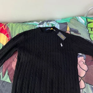 Svart tröja Polo Ralph Lauren - Svart  tröja från Polo Ralph Lauren med klassisk rund halsringning och vit broderad logga på bröstet. Tröjan har lång ärm och är gjord i ett mjukt material som passar perfekt till lager-på-lager-stil.