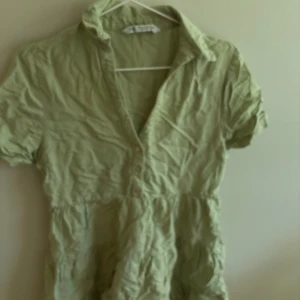 Ljusgrön kort klänning från Zara - Superfin ljusgrön kort klänning från Zara med krage, korta ärmar och knappar framtill. Tillverkad i ett lätt bomullstyg som passar perfekt för varma dagar. Avslappnad passform och snygg v-ringning.