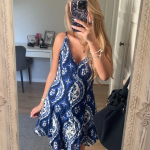 Blå och vit sommarklänning med mönster - Supersöt blå och vit kortklänning med blommigt mönster och tunna axelband. Klänningen har v-ringning, öppen rygg med snörning och en flowy passform. Aldrig använd💗💗💗