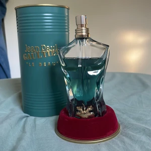 Jean Paul Gaultier Le Beau parfym - Parfymflaska formad som en manlig torso i genomskinligt glas med turkosblått innehåll. Kommer med en lyxig turkos metallburk med guldfärgad text och röd sammetsbas. En ikonisk och stilren doft för dig som gillar unika flaskor. Ungefär 60-65 ml kvar. I bra skick