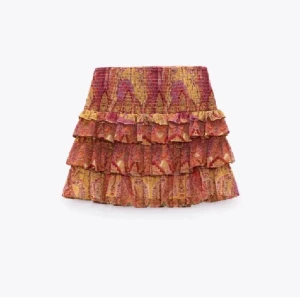 Färgglad volangkjol med mönster - Superfin kort kjol med flera volanger i orange, rött och gult. Kjolen har ett bohemiskt mönster och är perfekt för dig som gillar färg och rörelse. Sitter snyggt i midjan och ger en lekfull vibe till outfiten.