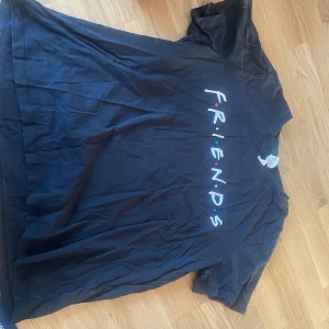 Svart Friends t-shirt från H&M - Svart t-shirt från H&M med Friends-tryck på bröstet och citat från serien på ryggen. Klassisk passform med rund hals och korta ärmar. Perfekt för dig som älskar tv-serien Friends och vill ha en chill och stilren look. Storlek XL. Baggy t shirt ifall man brukar ha S