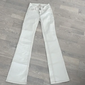 Vita bootcut jeans från Nelly - Snygga vita bootcut jeans från Nelly med ljusbruna kontrastsömmar och broderad detalj på bakfickorna. Klassisk femficksmodell med dubbla knappar framtill. Säljer pga att dom öf försmå.Jättebra skick använda några gånger.st 34