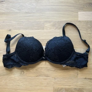 Svart push up bh från Cubus  - Säljer en svart push up bh med vacker blommig spets och vadderade kupor. Bh:n har justerbara axelband, hakknäppning bak och en liten metallcharm framtill. 