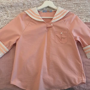 Rosa sailor-skjorta med vita detaljer - Superfin rosa sailor-skjorta med vita och ljusrosa ränder på krage och ärmslut. Skjortan har en bröstficka, knappar framtill och klassisk sjömanskrage. Materialet känns som bomull och är lätt och bekvämt. Perfekt för dig som gillar unik och söt stil. Den passar storlek S och M