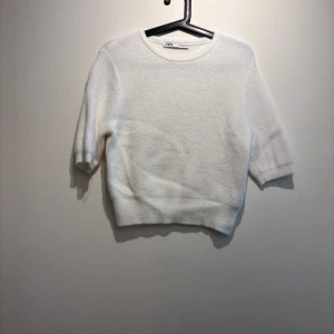 Vit stickad tröja från Zara - Supermjuk vit stickad tröja från Zara med rund hals och halvlånga ärmar. Tröjan har en enkel och clean look, perfekt att styla med jeans eller kjol. Materialet känns fluffigt och ger en cozy vibe.