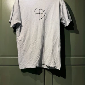 Vit Stone Island t-shirt med tryck - Vit t-shirt från Stone Island med stort svart logotryck på ryggen och mindre logga på bröstet. Klassisk rund halsringning och korta ärmar. Tillverkad i mjuk bomull för en skön känsla och clean look.