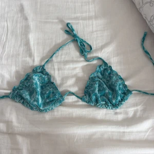 Turkos glittrig trekantsbikini - Supersnygg turkos trekantsbikini med glittrig yta och knyt i nacken och ryggen. Perfekt för strandhäng och poolparty! Tunn och lätt modell som ger en fräsch look. Det ingår även inlägg.