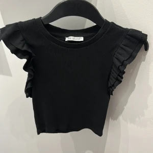 Svart volangtopp från ZARA - Supersnygg svart topp från ZARA med volangdetaljer på axlarna. Knappt använt. 