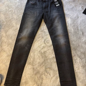 Svarta jeans Diesel D-Strukt - Snygga svarta jeans från Diesel, modell D-Strukt. Jeansen har en slim passform, klassisk femficksdesign och diskreta slitningar för en cool look. Tillverkade i stretchigt denim för extra komfort. Perfekta för dig som gillar stilrena och moderna jeans.