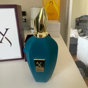 Xerjoff Erba Pura Eau de Parfum 100ml - Lyxig parfym från Xerjoff, Erba Pura, i en 100ml flaska. Flaskan är klädd i sammetsliknande turkost material med guldfärgad metallkork och gulddetaljer. Kommer i elegant lila och vit box med guld- och blå accenter. Perfekt för dig som gillar exklusiva dofter. Priset är inte hugget i sten