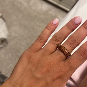 Bred guldtonad ring med stenar - Säljer en bred ring i guldton med glittrande små stenar runt hela bandet. Ringen har en rundad form och ger ett lyxigt intryck, perfekt för dig som gillar att sticka ut med accessoarer.