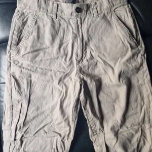 Beiga linnebyxor från H&M, relaxed fit - Snygga beiga byxor från H&M i relaxed fit med klassisk knappstängning och fickor på sidorna. Tillverkade i en skön mix av 50% linne och 50% bomull, perfekta för en chill och avslappnad stil. Passar dig som gillar loose fit och naturliga material.