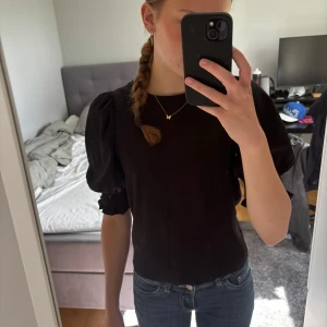 Svart blus med puffärm från Lindex - Supersnygg svart blus från Lindex med puffiga ärm och smockdetalj vid ärmslut. Perfekt till jeans eller kjol för en trendig look. Kommer ej till användning längre så därför säljer jag den!💗